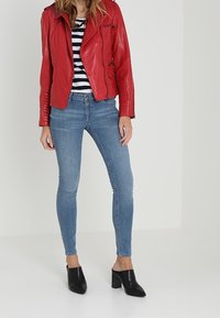 Giubbotto in pelle rossa per moto con dettagli in zip, maglietta a righe bianca e nera, jeans skinny blu e mule con tacco aperto neri.