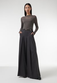 Grijze long-sleeve top en hoogwaardig, wijde zwarte broek met plooien en een riem met een gouden gesp. De broek heeft zijzakken.