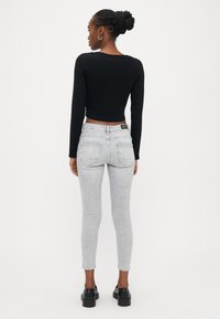 Μαύρο cropped τοπ με μακριά μανίκια, συνδυασμένο με ανοιχτό γκρι στενά τζιν. Το τζιν διαθέτει πέντε τσέπες και αδιάκοπο σχέδιο. Μαύρα παπούτσια ολοκληρώνουν το σύνολο.