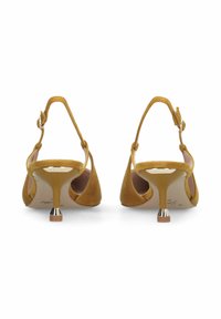 Paire d'escarpins slingbacks en daim jaune moutarde avec talons stiletto étroits de hauteur moyenne et brides réglables à la cheville sur fond blanc.