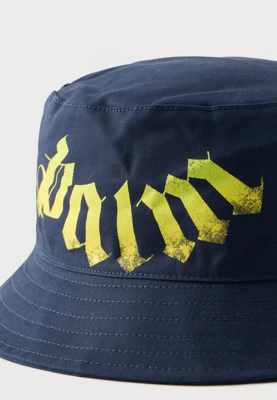 Καπέλο τύπου bucket σε ναυτικό μπλε χρώμα με κίτρινα γοτθικά γράμματα σε στυλιζαρισμένη μορφή τυπωμένα στο μπροστινό μέρος.