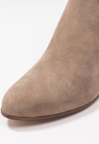 Beżowe zamszowe botki za kostkę z noskiem w szpic i gładką teksturą, z niskim, drewnianym obcasem oraz bezszwowym designem.