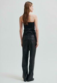 Černý bezramínkový top se smockovanou texturou, který je spojen s černými koženými kalhotami s vysokým pasem, nabízejícími elegantní siluetu a decentní zadní kapsy.