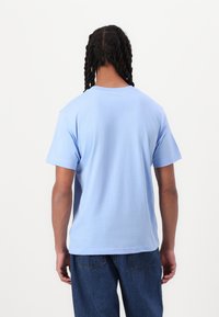 T-shirt en coton bleu clair à manches courtes, col rond et texture lisse ; porté avec un jean en denim bleu.