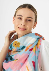 Foulard léger multicolore à motif floral en tissu doux. Il présente une base bleue avec des fleurs jaunes et roses ainsi que des motifs géométriques. Les bords sont effilochés.