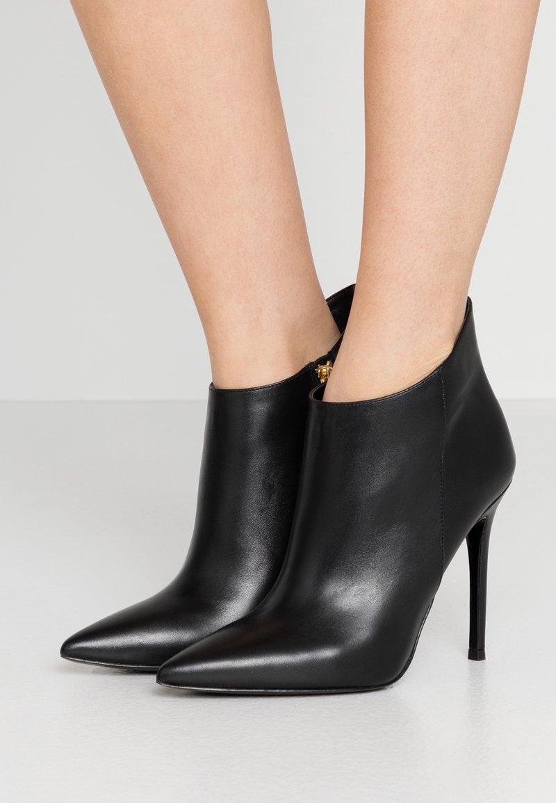Bottines noires en cuir avec un nez pointu, un talon aiguille haut et un détail de fermeture éclair à l'arrière. Texture lisse avec un design élégant.