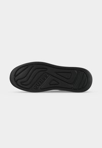 Semelle de chaussure noire avec des motifs géométriques et « GUESS » embossé près du centre sur un fond clair uni.