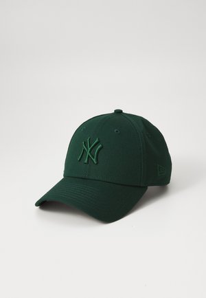 Mørkegrøn baseballkasket med buet skygge og broderede overlappende bogstaver på frontpanelet mod en ensfarvet lys baggrund.