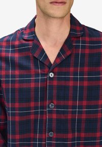 Rutig skjorta i röd, marinblå och vit. Har en notch-krage, knäppning fram och mjukt tyg med ett rutigt mönster.