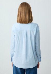 Lichtblauwe langgewicht shirt met een relaxte pasvorm. Bevat een achterstuk en knoopmanchetten. Zachte stof, gebogen zoom.