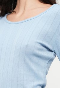 Ανοιχτό μπλε ριμπ πλεκτό μακρυμάνικο τοπ με στρογγυλή λαιμόκοψη. Διαθέτει κάθετες ρίγες και διακριτική υφή με μικρά διακριτικά μοτίβα.