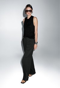 Top nero senza maniche con scollatura drappeggiata, abbinato a pantaloni larghi neri a gamba larga. Tessuto leggero e design minimalista.