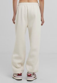 Witte sweatpants gemaakt van zachte stof, met een elastische tailleband en een relaxte pasvorm. Gecombineerd met Nike-sneakers in wit, roze en bordeauxrood.