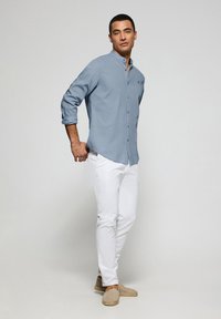 Ljusblå skjorta med knappar och långa ärmar, i kombination med vita smala byxor och beigea slip-on skor. Enkelt design och klassiska färger.