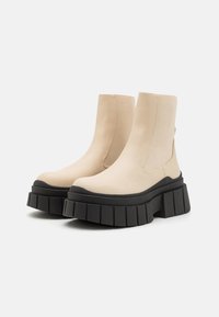 Beige ankle boots made of smooth leather with elastic side panels and a thick black platform sole featuring a ridged texture.