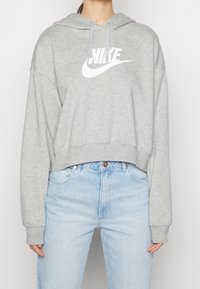 Sudadera corta gris con un gran logo blanco de Nike en el frente, que cuenta con capucha con cordón y una tela suave y texturizada.
