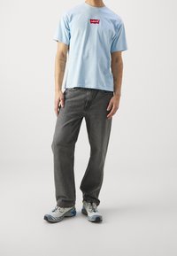 Světle modré bavlněné tričko s červeným logem Levi's, spárováno s tmavě šedými džínami a šedými sportovními botami s modrými akcenty.