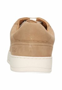 Tan mockasinsneakers med rund tå, snörning, vit gummisula och kontrasterande innertyg. Inga synliga logotyper.