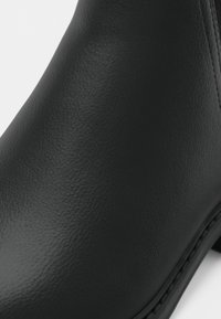 Gros plan sur une bottine en cuir noir à texture lisse avec une couture visible le long du bord de la semelle.
