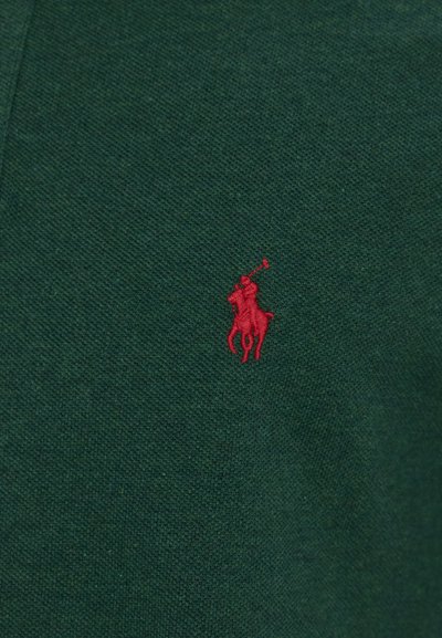 Grön bomullsplagg med en strukturerad yta, prytt med en liten röd broderad logotyp av en ryttare.
