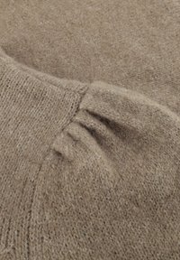 Lichtbruin gebreid sweaterstof met een zachte textuur, met geplooide details op de schouder en een geribde halslijn.