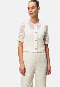 Set di cardigan e pantaloni all'uncinetto color crema, con scollatura rotonda, maniche corte e bottoni decorativi con un design testurizzato e a motivi.
