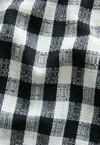 Material textil alb-negru cu model în carouri, având o țesătură texturată și pătrate alternative cu modele și texturi diferite ale firelor.
