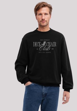 Schwarzer Pullover mit langen Ärmeln und Rundhalsausschnitt, versehen mit weißem Text, der "STOLZES MITGLIED DES DECKCHAIR-Clubs gegründet 1999" liest, sowie einer Grafik eines Stuhls.