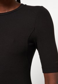 Haut noir à manches courtes côtelé avec un col rond, présentant une coupe ajustée et des détails de couture subtils. Le matériau semble lisse et extensible.