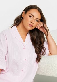 Lyhythihainen, kauluksellinen paita vaaleanpunaisena valkoisilla pystyraitoilla. Sisältää napit ja yhden taskun vasemmassa rinnassa. Pehmeä pinta.