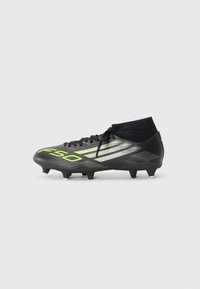 Zwarte voetbalschoenen met groene en zilveren details, voorzien van een hoge enkeldesign en zes studs op de buitenzool voor grip.