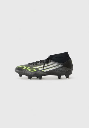 Black soccer cleat with green and silver detailing, featuring a high ankle design and six studs on the outsole for traction.
