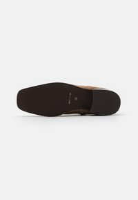 Chaussure en daim beige avec un bout pointu et une semelle en caoutchouc noir. Présente une texture lisse et un petit talon. Taille indiquée comme 36.