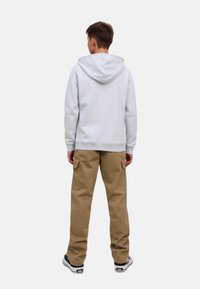 Ljust grå hoodie med dragkedja i huvan, tillsammans med khaki cargobyxor med sidofickor och svarta sneakers med vita sulor.