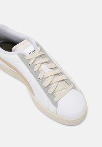 Vita sneakers med beige och ljust grå detaljer, med en strukturerad ovandel, snörningsdesign och en gummisula med ett subtilt mönster.