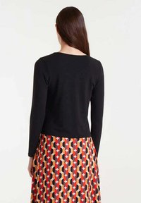 Top negro de manga larga con escote redondeado, combinado con una falda estampada que presenta formas geométricas en rojo, amarillo y negro.