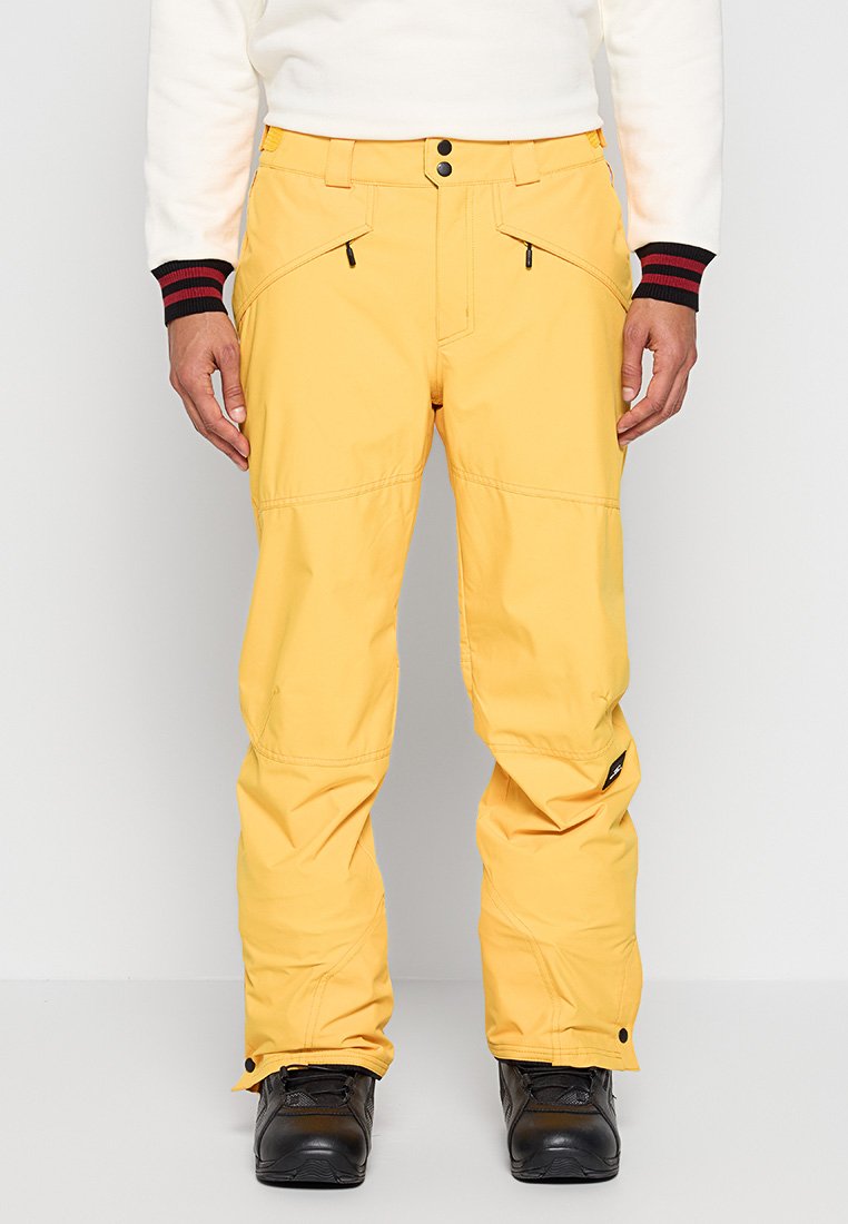 Helle gelbe Skihosen mit glatter Textur, Reißverschluss-Taschen, verstärkten Nähten und leicht zulaufenden Beinen, kombiniert mit schwarzen Stiefeln.