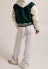 Vihreä ja kermanvärinen yliopistotakki hupulla, jossa on resorit hihansuissa ja helmaosassa, yhdistetty harmaisiin verkkareihin ja lenkkareihin.