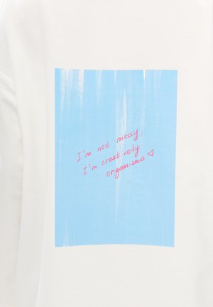 Sweat-shirt blanc avec un motif bleu strié et un texte rose disant : "Je ne suis pas désordonné, je suis créativement organisé."