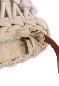 Bolsa de algodón con cordón, detalle de cuerda trenzada, cremallera metálica y asa de cuero tostado.