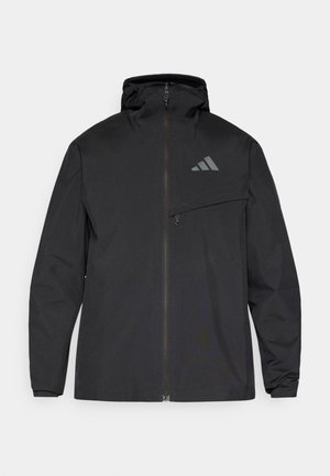 Veste imperméable noire avec fermeture éclair à l'avant, capuche réglable et poche poitrine. Présente un logo discret sur le côté supérieur gauche.