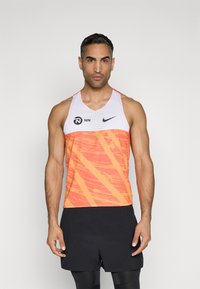 Oranž ja valge sportlik tank top tekstuuriga mustriga, ümarate kaelaaugu ja brändingu detailiga rinnal. Mustad lühikesed püksid siledast materjalist.
