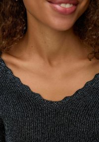 Suéter negro con escote con volantes y hilos metálicos. Primer plano de la textura de la tela y detalles del escote.