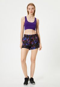 Lilla atletisk crop top og sorte shorts med et livligt abstrakt mønster i blå og rød. Mesh og elastisk taljedetalje.