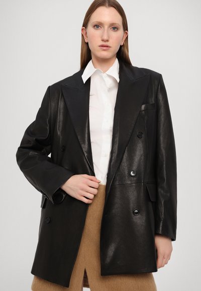 Melnas ādas divrindas žakete ar lielām atlokām, teksturētu apdari un divām priekšējām pogām. Saskaņota ar baltu krekliņu un brūnām svārkiem.