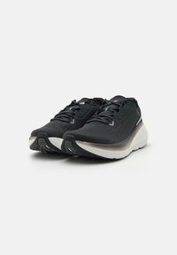 Des chaussures de sport noires avec une tige en maille texturée, un col rembourré, et une semelle bicolore présentant un profil en caoutchouc noir et une semelle intermédiaire blanche.