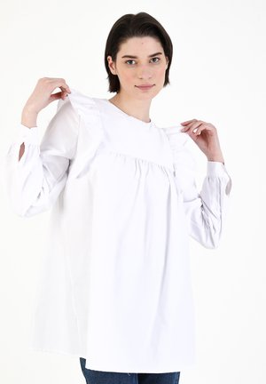 White long-sleeve blouse with a high neckline, ruffled shoulder accents, and slight gather at the bust, featuring buttoned cuffs.