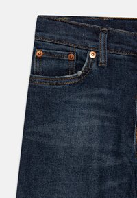 Tmavě modré džíny z denimu s měděnými nýty, viditelným prošíváním a malou přední kapsou. Měkká textilie a klasický design s pěti kapsami.