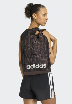 Black and brown leopard-print backpack with top handles, front zip pocket, and white "adidas" logo on the bottom. Textured fabric design.