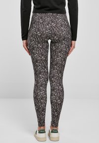 Leggings neri con un motivo astratto bianco, caratterizzati da una vestibilità aderente e una texture liscia. Indossati con sneaker bianche che mostrano accenti verdi.